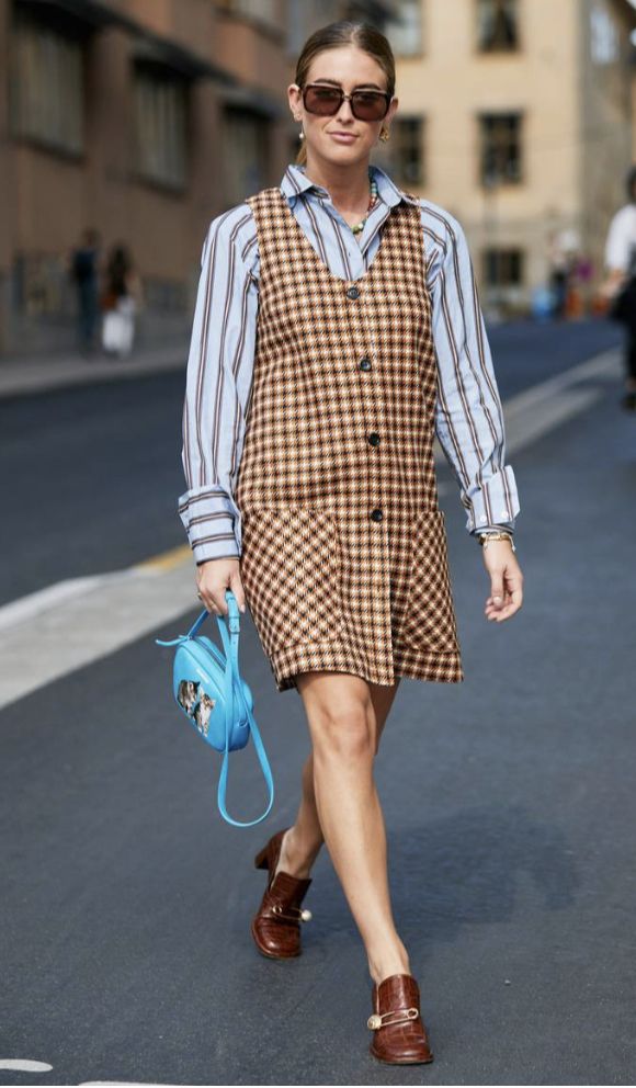 Mulher caminhando usando uma blusa listrada, vestido xadrez e bolsa azul 
