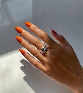 Mão branco com anel e unha laranja queimado