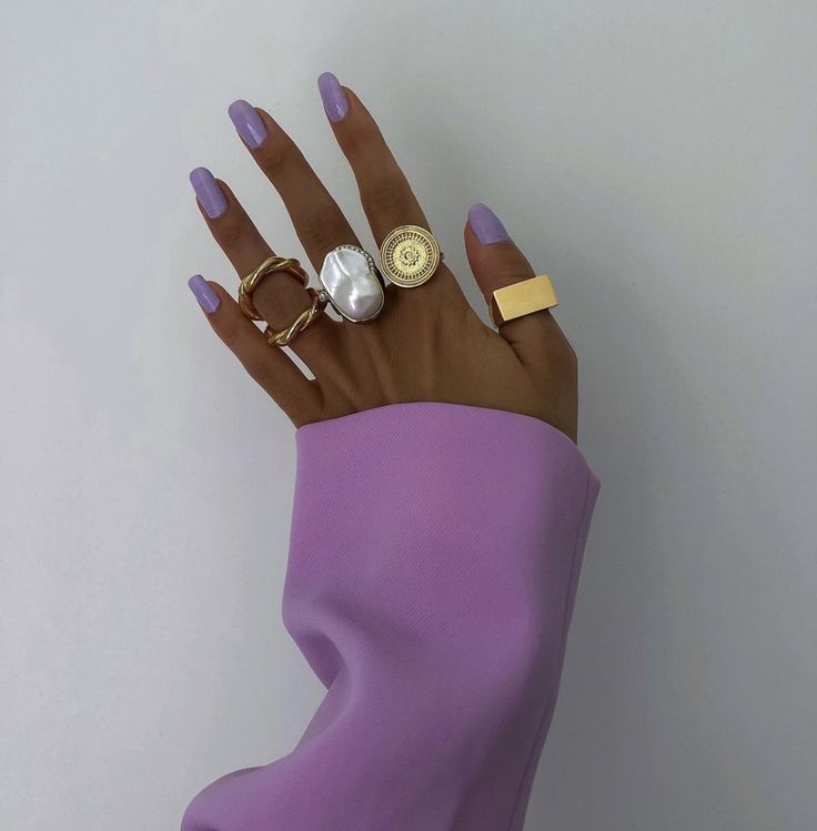 Mão com casaco lilás, anéis e unha lilás