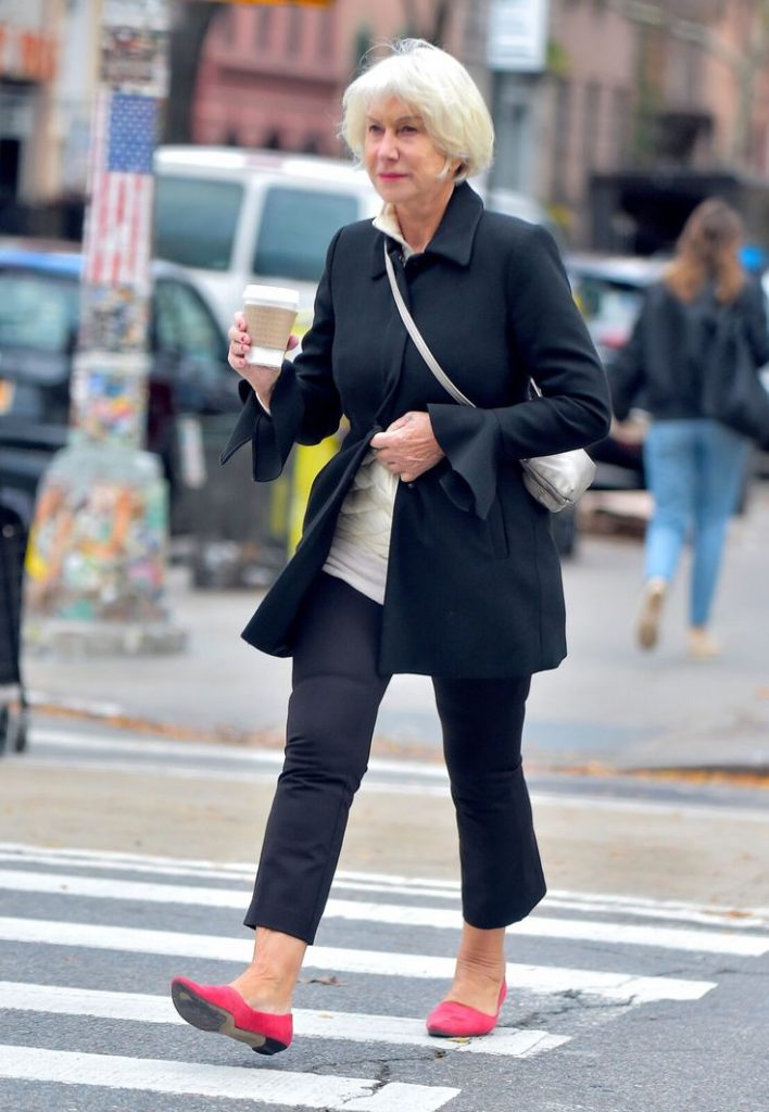 Mulher de 60 anos caminhando na rua com casaco preto e cabelo curto branco