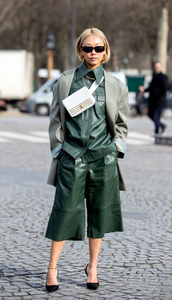 Mulher asiática parada na rua. Ela veste look monocromático verde esmeralda e scarpin preto