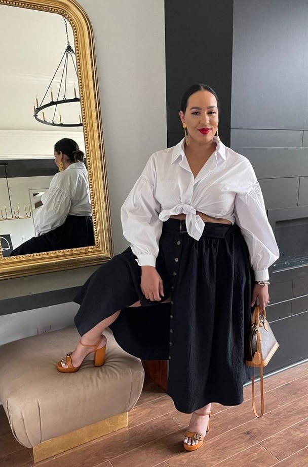 Mulher branca, plus size, com saia preta longa e com camisa branca