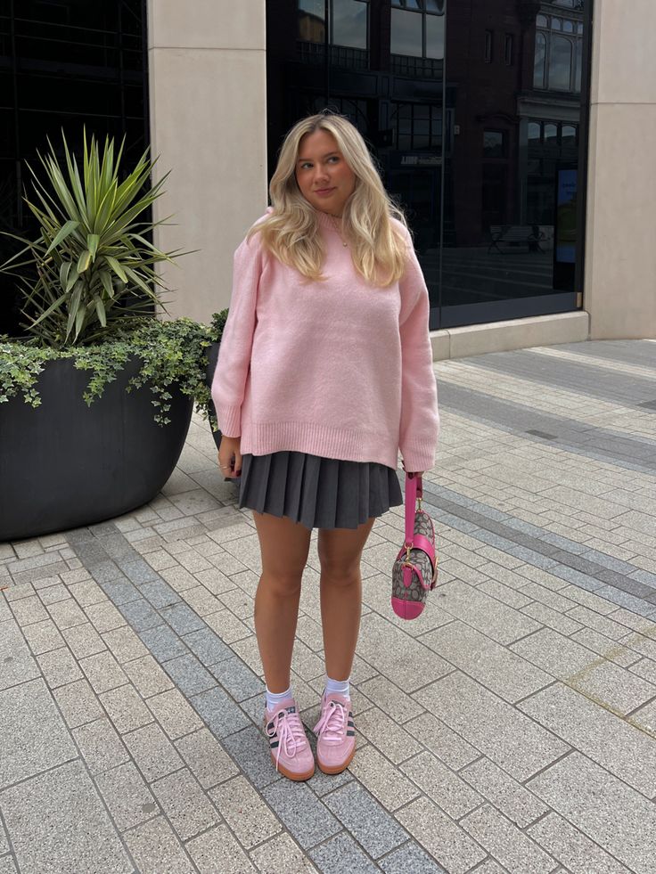 Mulher loira usando tricô rosa pastel, minissaia plissada cinza e tênis Adidas esportivo