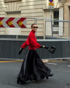 Mulher caminhando na rua. Ela veste tricô vermelho intenso, saia preta e bota