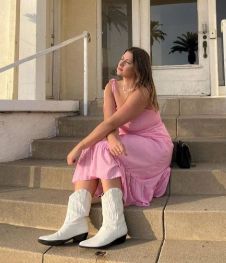 mulher sentada em escada usando vestido rosa e bota western