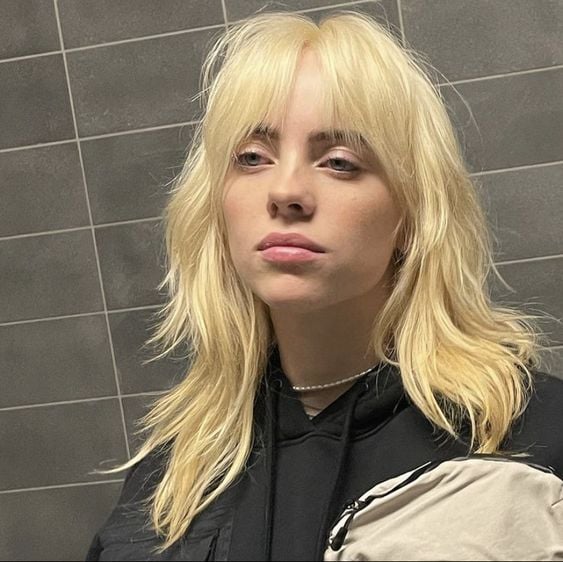Billie Eilish com cabelo loiro, longo e com franja, no estilo wolf cut