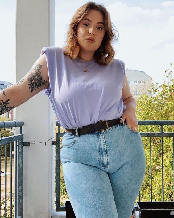 Mulher branca e jovem com cabelo médio no estilo bob com franja, usando calça jeans, cinto e blusa lilás