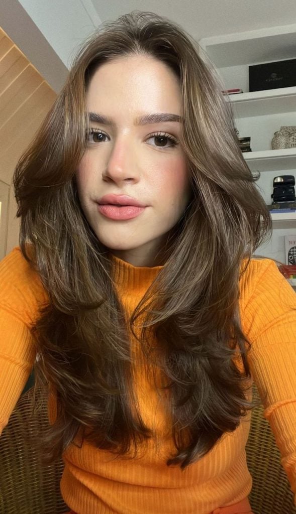 Mulher com blusa alaranjada e cabelo longo em camadas