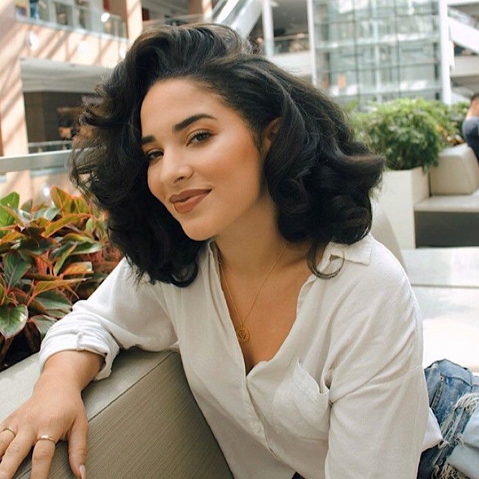 Mulher com blusa branca e cabelo cacheado preto