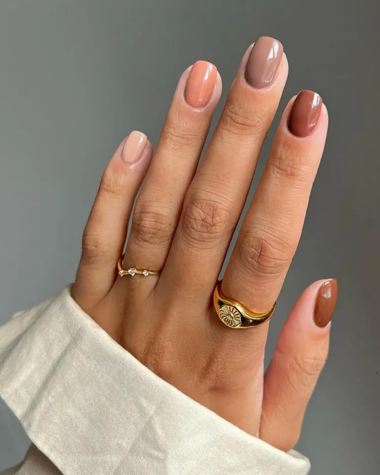 Mão branca com camisa dobrada, anéis e chocolate nail degradê