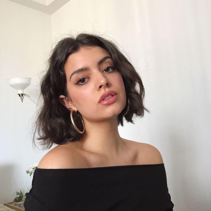 Mulher branca e jovem com cabelo curto no estilo french bob, com brinco de argola e blusa sem alça