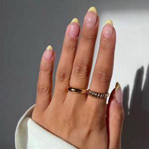 Mão branca com manga branca, anéis e unha francesinha amarela