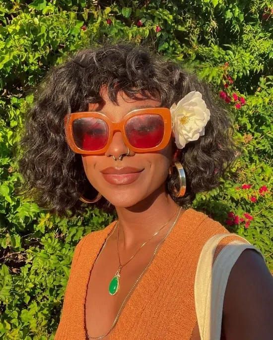 Mulher negra com cabelo curto com franja, usando óculos de sol e flor no cabelo
