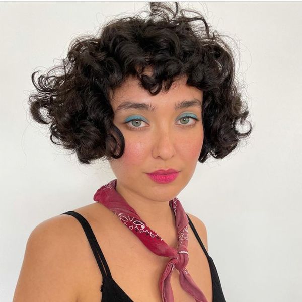 Mulher com regata preta, lenço no pescoço e cabelo cacheado micro bob