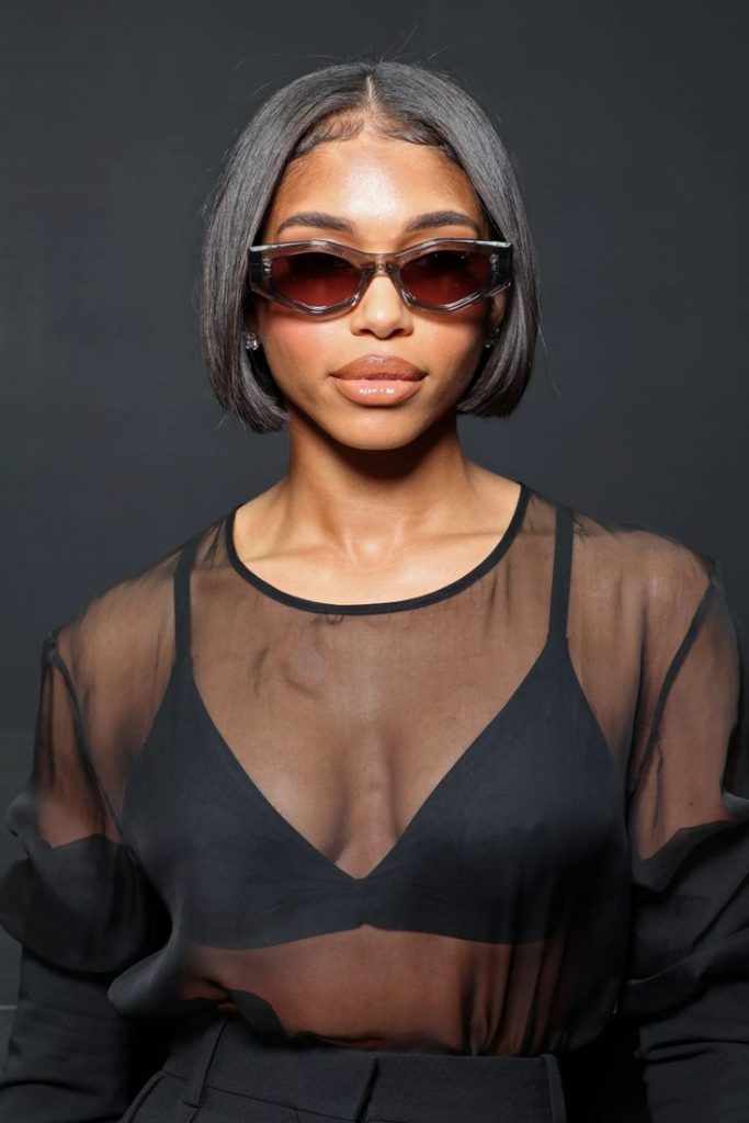 Mulher com top preto, blusa preta transparente, óculos escuro e cabelo preto short bob 