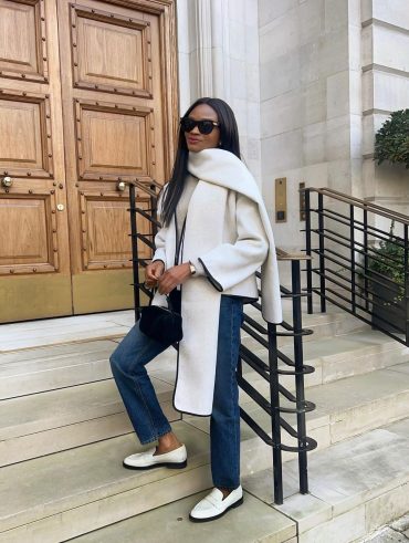 Mulher não branca. Ela usa cachecol off-white, casaco off-white, calça jeans reta e loafer branco
