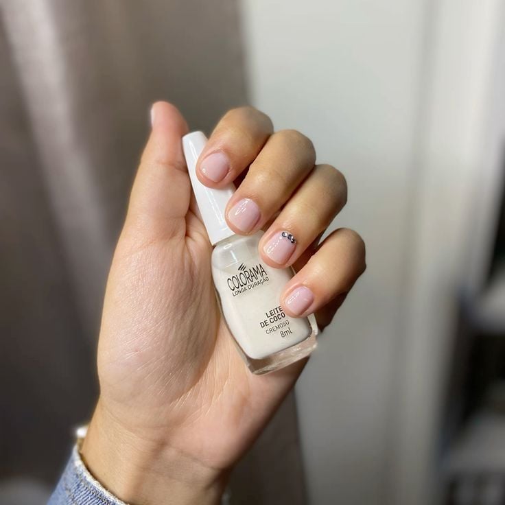 Mão branca segurando com esmalte branco, com unha branca decorada