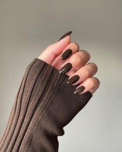 Mão branca com manga marrom, anel e unha chocolate