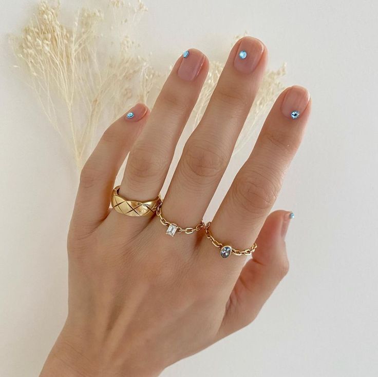 Mão branca com anéis e unha transparente com strass azuis 