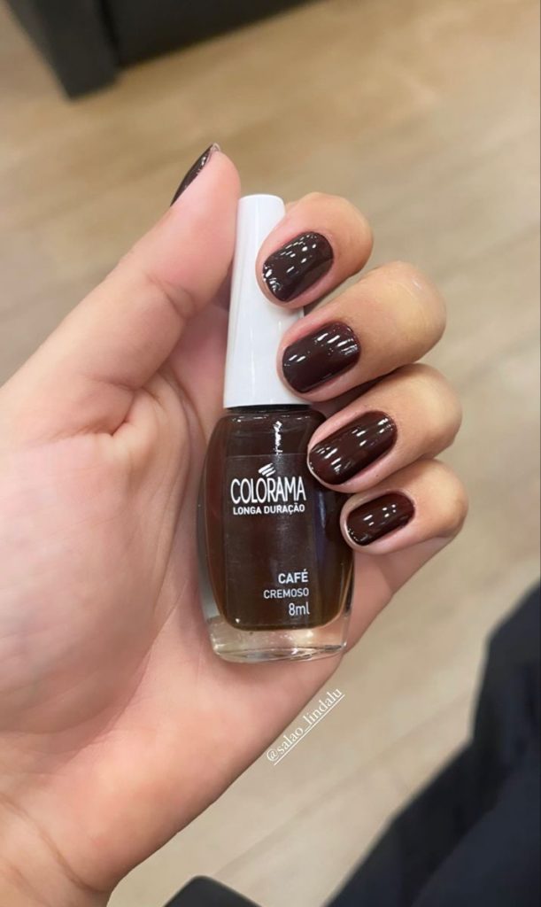 Mão branca segurando o esmalte Café da Colorama e com as unhas de mesma cor