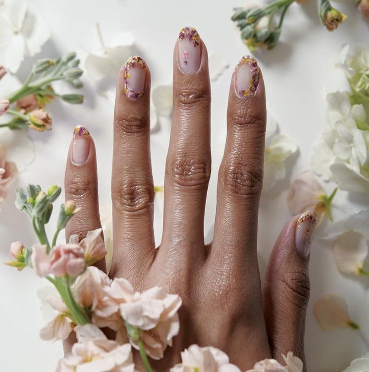 Mão aberta com flores no fundo e na frente, e unha decorada com flores