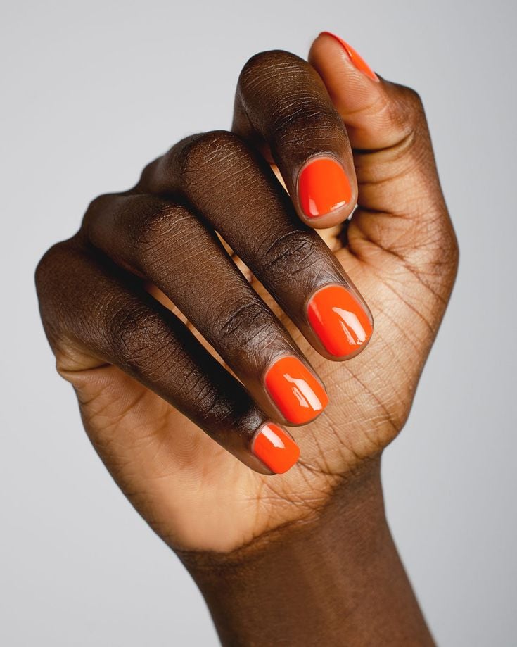 Mão negra encurvada com esmalte laranja