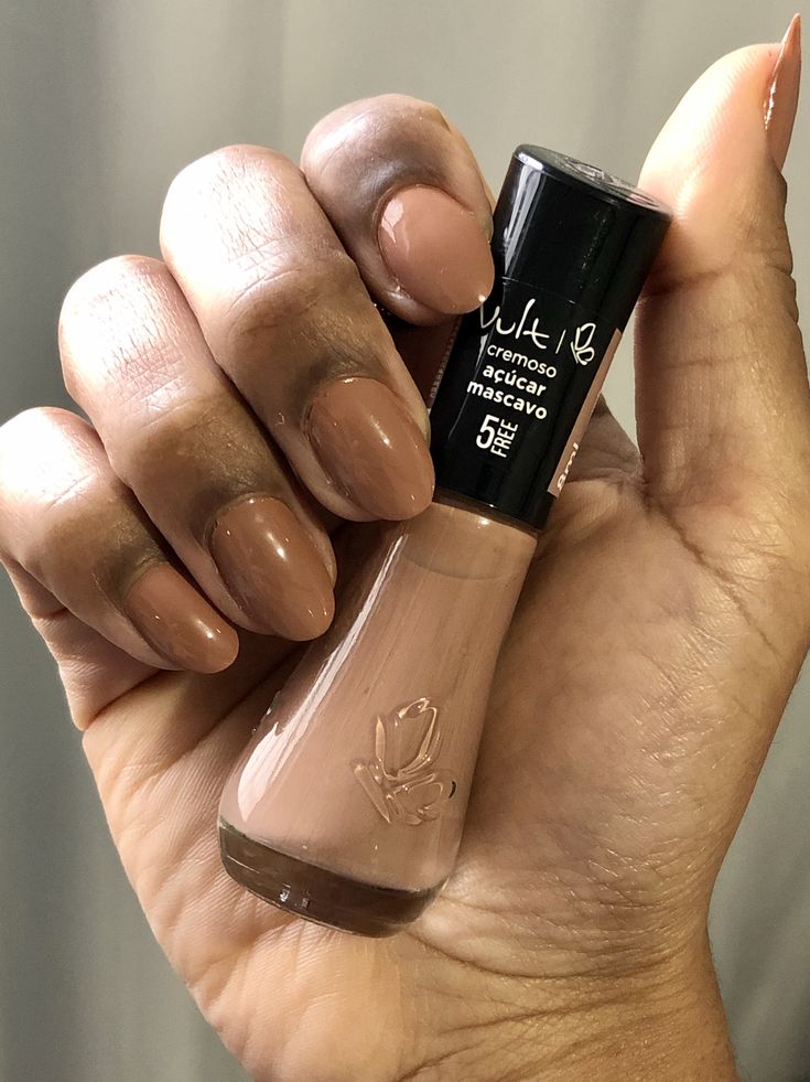 Mão segurando o esmalte açúcar mascavo da Vult, com as unhas na mesma cor