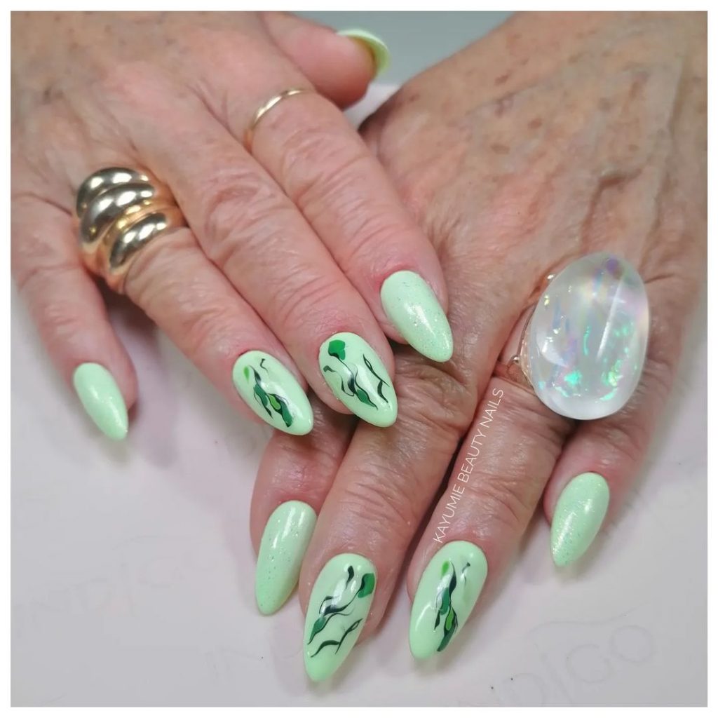 Mão branca de mulher mais velha com anéis, e unha verde menta decorada