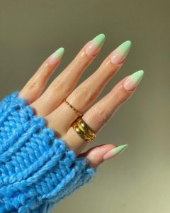 Mão branca com tricot azul, anéis dourados e unha ombré verde menta