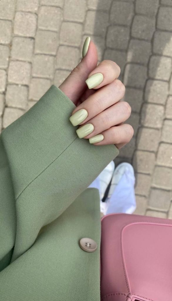 Mão branca encurvada com manga verde e unha verde quadrada