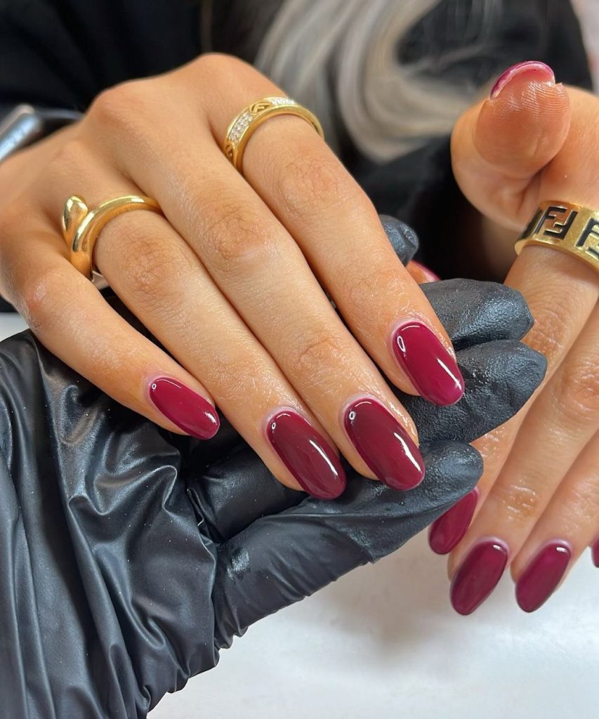 Mão branca apoiada em uma mão com luva preta, com anéis e unha amendoada vermelho cereja 