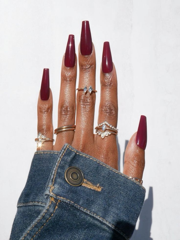 Mão negra com manga de jaqueta jeans, anéis e unha bailarina vermelho cereja