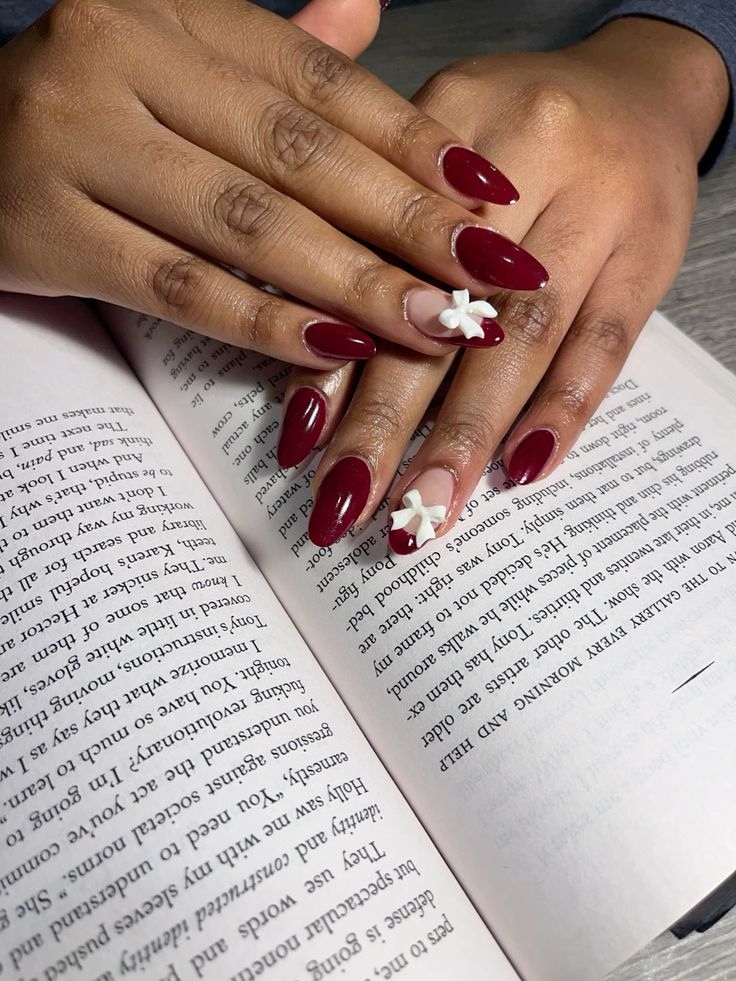 Mãos negras apoiadas em um livro, com a unha vermelho cereja e um laço branco 3D