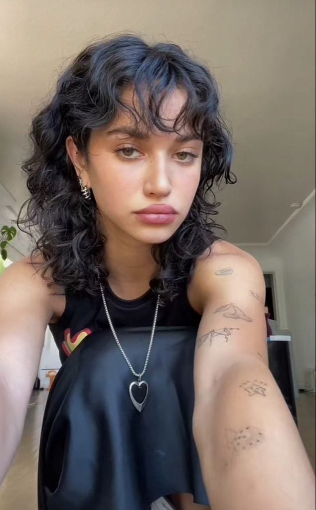 Mulher com cabelo preto, cacheado, longo e com franja, no estilo wolf cut