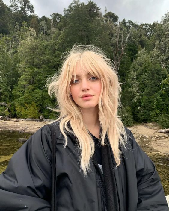 Mulher com cabelo loiro, longo e com franja, no estilo wolf cut