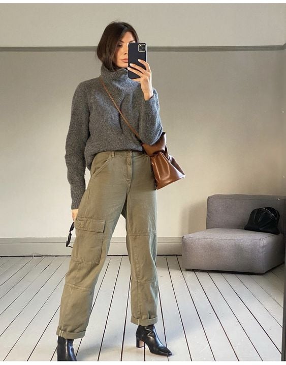 Mulher usando suéter cinza, jeans verde e botas de salto alto