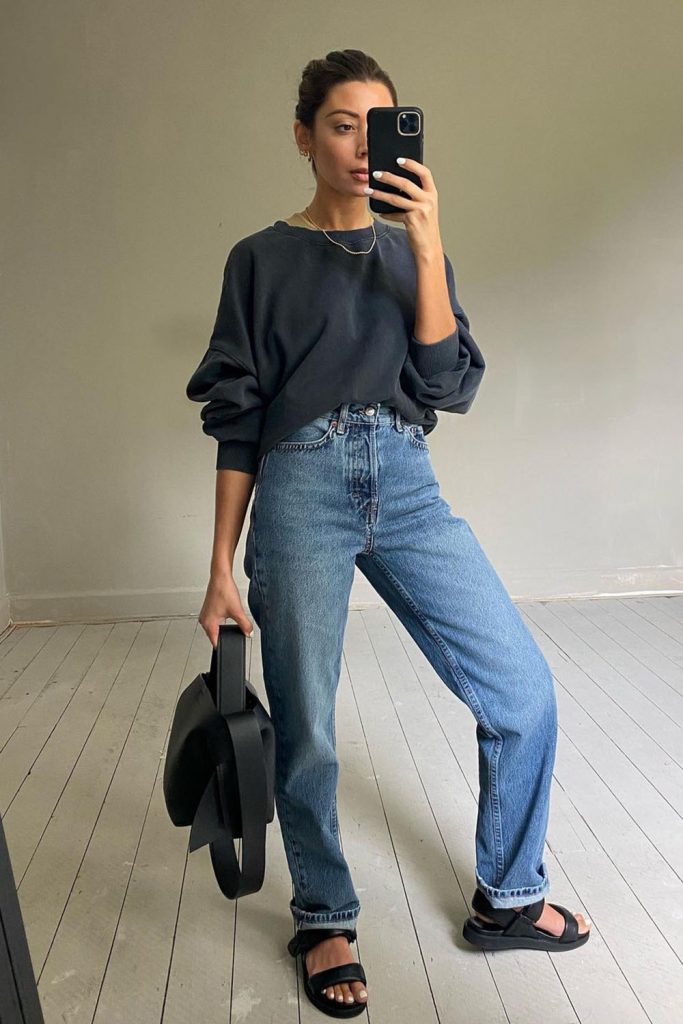 Mulher usando moletom cinza e calça jeans reta com papete preta