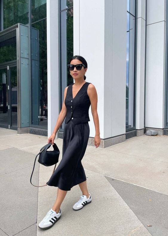 Mulher usando colete preto, saia de cetim preta e tênis