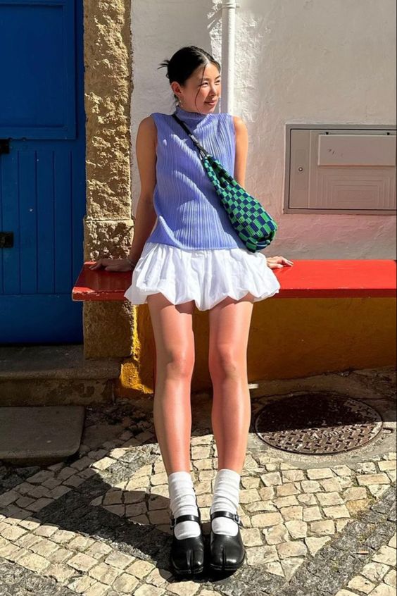 Mulher usando regata lilás, saia balonê branca e sapato boneca
