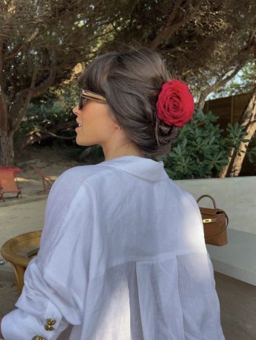 Mulher branca de cabelo moreno usando acessório de flor vermelha