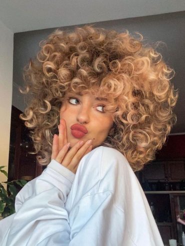 Mulher branca com blusa branca comprida e cabelo cacheado loiro