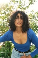 Mulher com cabelo preto, cacheado e médio na altura dos ombros.