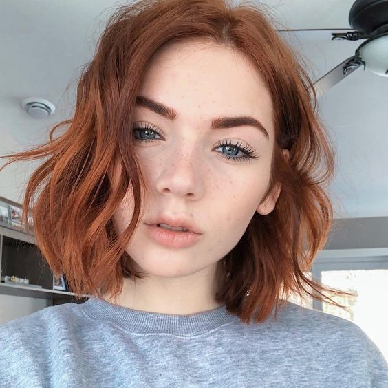 Mulher branca com camisa cinza e cabelo curto ruivo repicado
