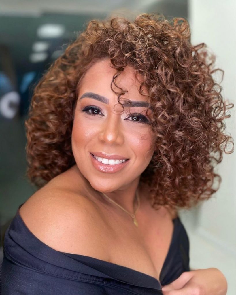 Mulher negra com blusa preta, maquiagem e cabelo ruivo doce de leite cacheado