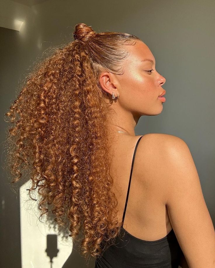 Mulher negra de perfil com regata preta e cabelo meio preso ruivo dourado