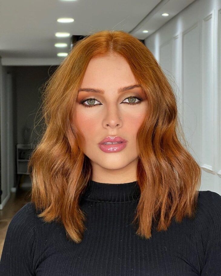 Mulher branca com blusa preta, maquiagem e cabelo curto ruivo nude
