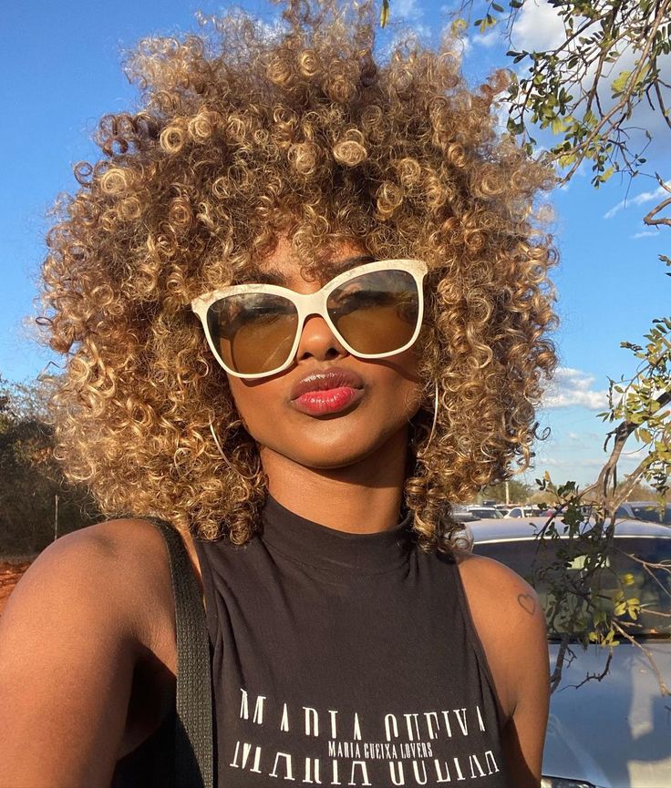 Mulher negra com cabelo crespo e castanho, iluminado com loiro mel