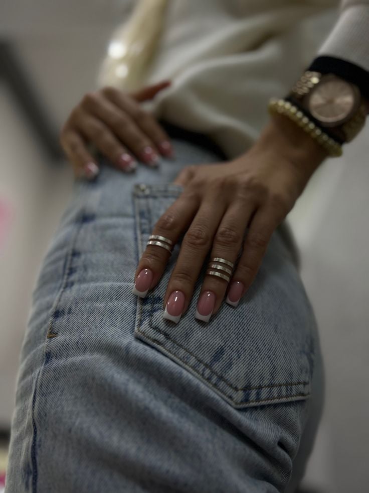 Mão negra apoiada na calça, com anéis e unha francesinha branca tradicional