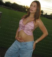 Hailey Bieber com top de borboleta rosa. Ela está grávida e segurando a barriga.