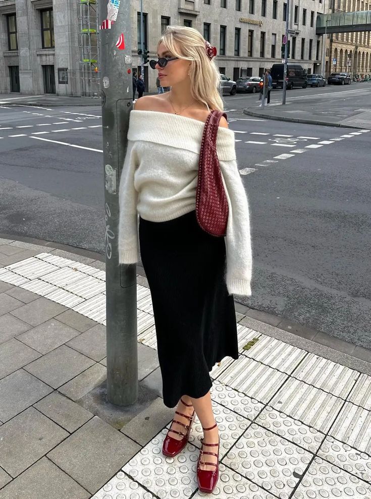 Linda. A influenciadora de moda usa acessório no cabelo, blusa ombro a ombro off-white, saia midi preta e sapato boneca e bolsa vermelho cereja